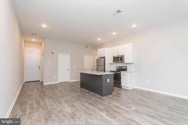 kitchen featuring a kitchen island with sink, white cabinets, stainless steel appliances, and light wood-type flooring