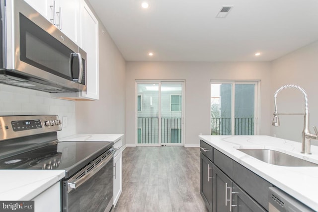 kitchen with sink, light wood-type flooring, appliances with stainless steel finishes, light stone counters, and white cabinetry