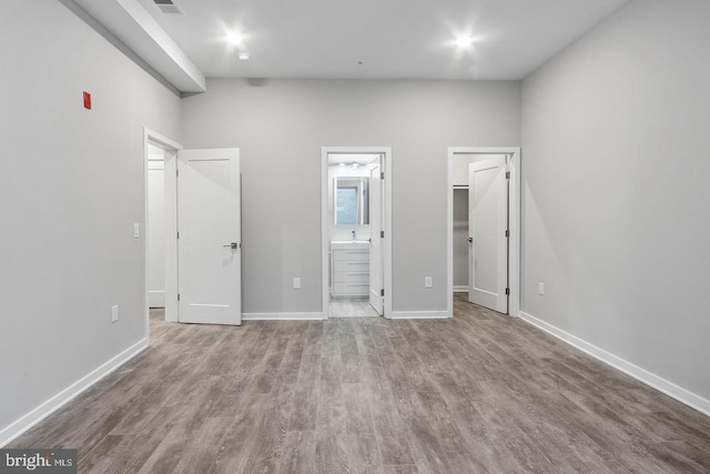 unfurnished bedroom with connected bathroom, hardwood / wood-style flooring, and a spacious closet