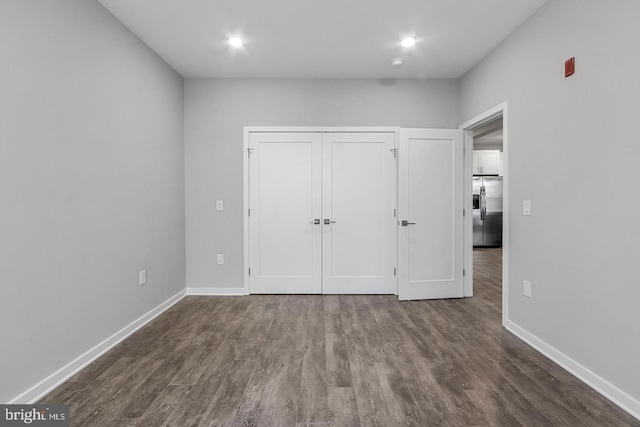 unfurnished bedroom with stainless steel fridge and dark wood-type flooring