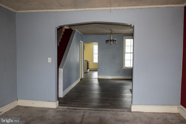 empty room featuring a notable chandelier, crown molding, and dark wood-type flooring