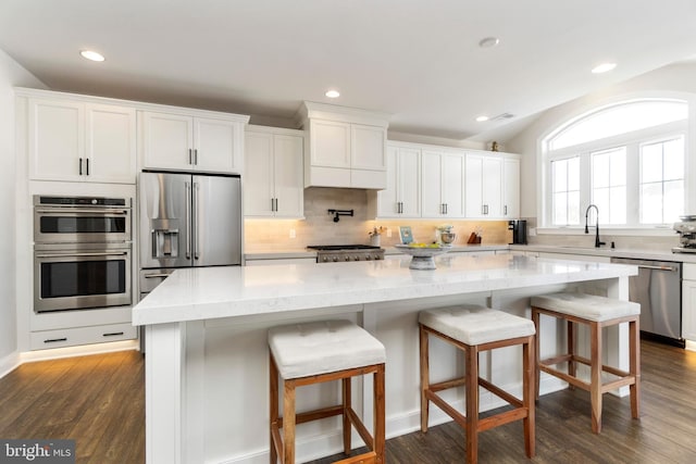 kitchen with white cabinets, light stone counters, dark hardwood / wood-style flooring, a kitchen island, and appliances with stainless steel finishes