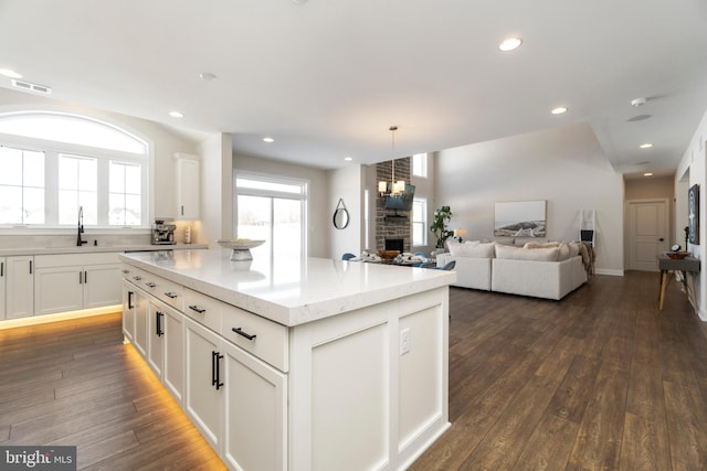 kitchen featuring sink, a fireplace, a kitchen island, dark hardwood / wood-style flooring, and white cabinetry