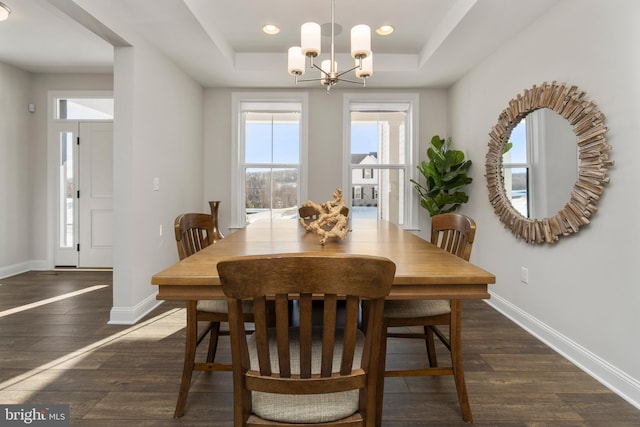 dining area with a tray ceiling, dark hardwood / wood-style floors, and an inviting chandelier