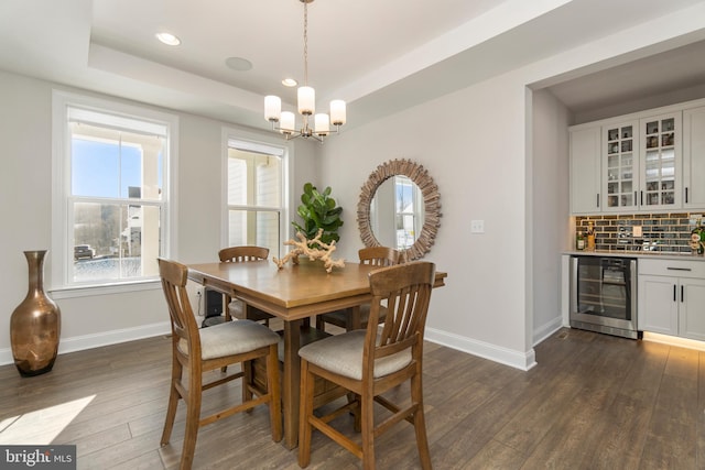 dining room with dark hardwood / wood-style flooring, a tray ceiling, beverage cooler, indoor bar, and a chandelier