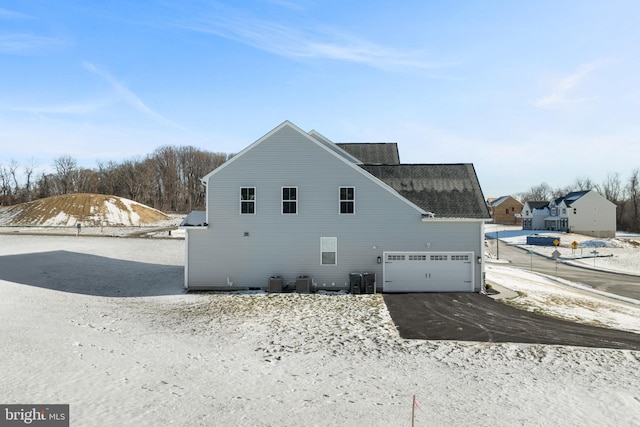 snow covered property with central AC and a garage