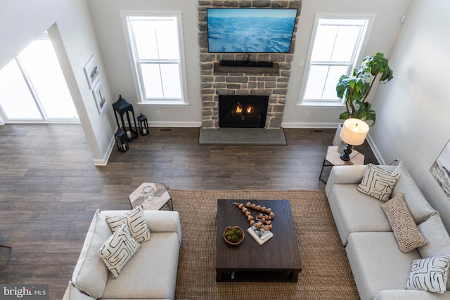 living room with a stone fireplace and dark wood-type flooring