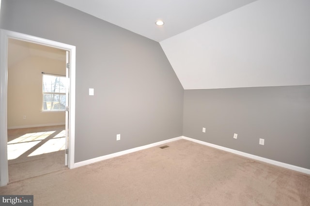 additional living space featuring light colored carpet and vaulted ceiling