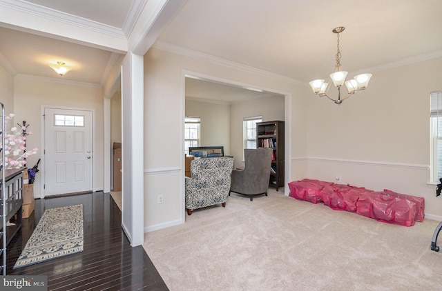 carpeted entryway featuring baseboards, ornamental molding, wood finished floors, and an inviting chandelier