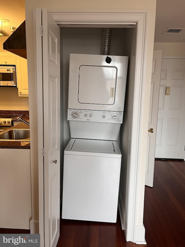 laundry area with sink, stacked washer / drying machine, and dark wood-type flooring