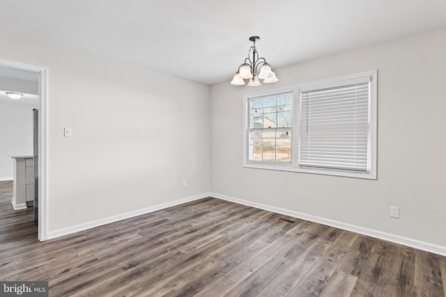 empty room with dark hardwood / wood-style flooring and an inviting chandelier