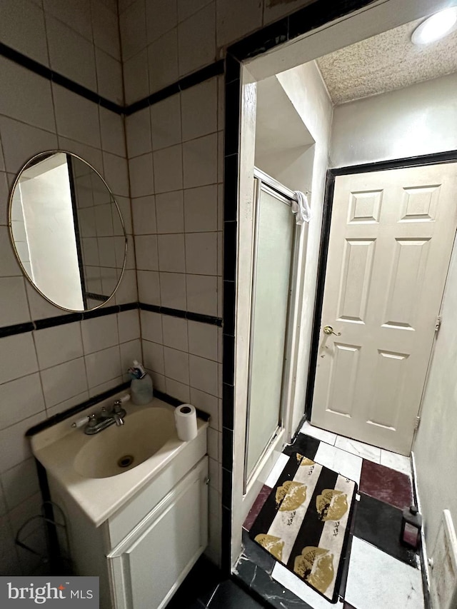 bathroom featuring tile patterned flooring, vanity, a shower with shower door, and tile walls