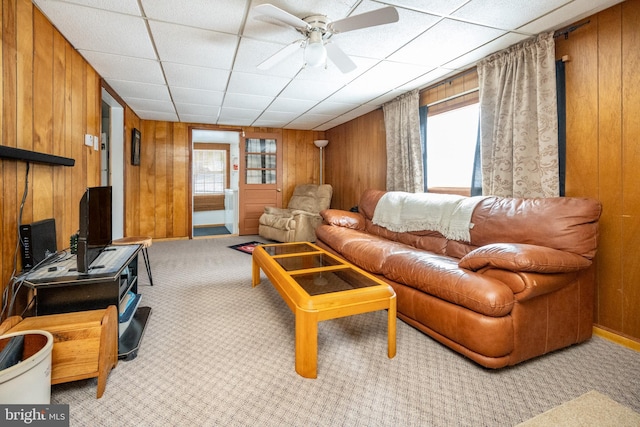 living room with ceiling fan, light colored carpet, a drop ceiling, and wooden walls