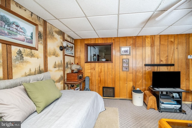 carpeted bedroom featuring a drop ceiling and wood walls