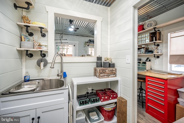 kitchen with ceiling fan, sink, wood walls, and hardwood / wood-style flooring