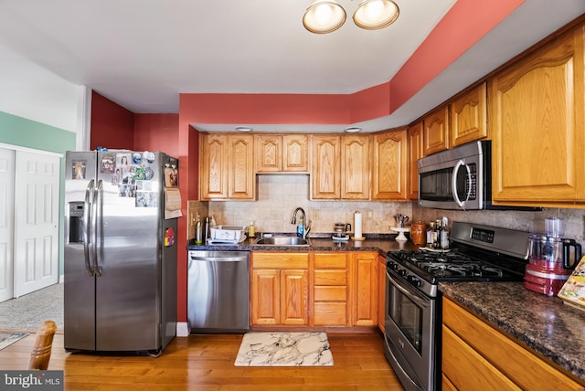 kitchen with light wood-type flooring, backsplash, stainless steel appliances, sink, and dark stone countertops