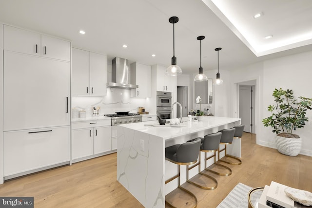 8551 Connecticut Ave Unit 210, Chevy Chase, MD 20815 - kitchen with a kitchen island with sink, white cabinets, wall chimney exhaust hood, light wood-type flooring, and decorative light fixtures