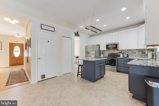 kitchen with stainless steel appliances, sink, white cabinets, a breakfast bar area, and a kitchen island