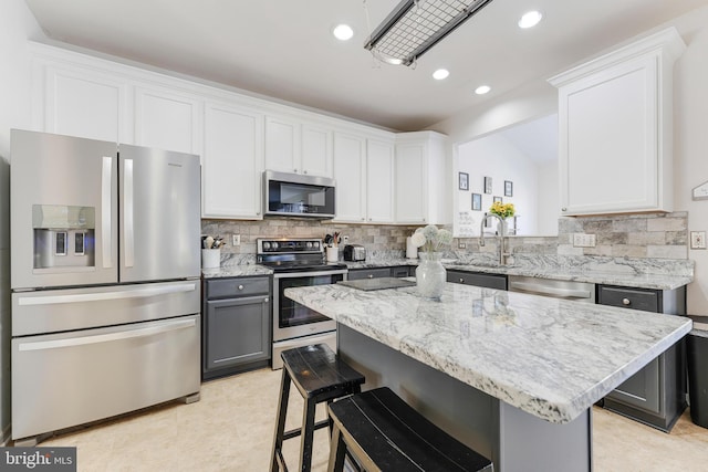 kitchen with a center island, backsplash, white cabinets, appliances with stainless steel finishes, and a kitchen breakfast bar