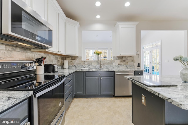 kitchen featuring gray cabinetry, stainless steel appliances, light stone countertops, white cabinets, and tasteful backsplash