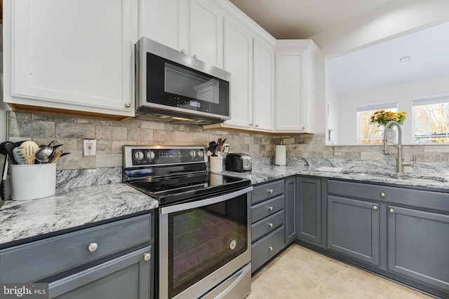 kitchen with gray cabinets, stainless steel appliances, light stone counters, sink, and white cabinetry