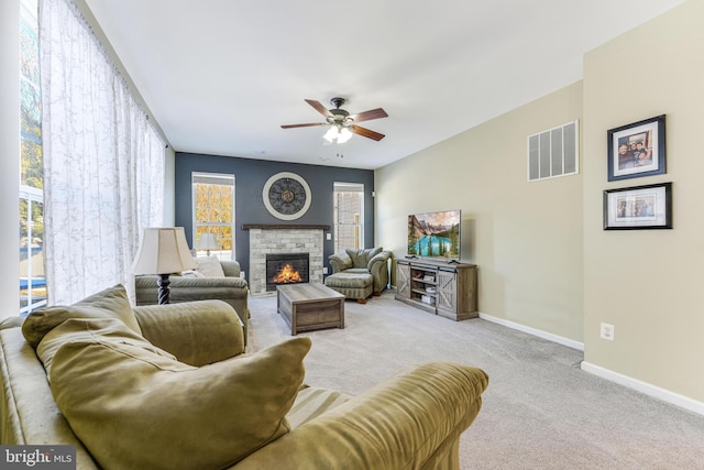 carpeted living room featuring ceiling fan and a stone fireplace