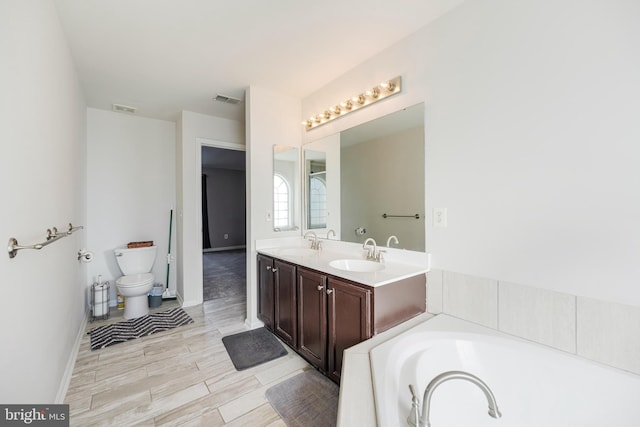 bathroom featuring a relaxing tiled tub, vanity, and toilet