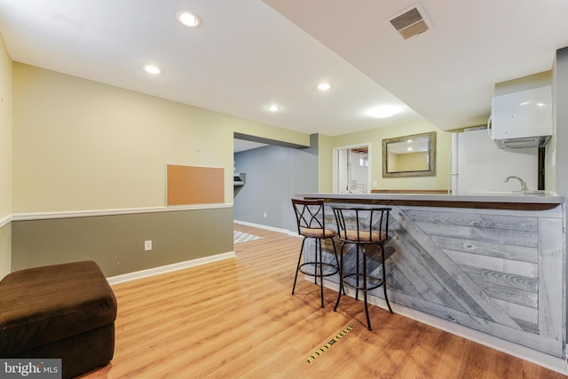 kitchen with kitchen peninsula, a wall mounted AC, light hardwood / wood-style floors, a breakfast bar, and white cabinets