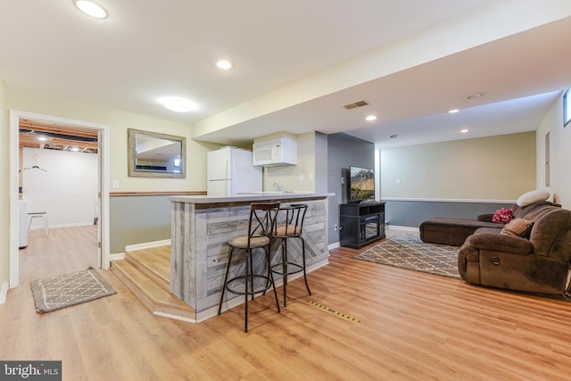 kitchen featuring kitchen peninsula, white fridge, light hardwood / wood-style floors, a breakfast bar, and white cabinetry