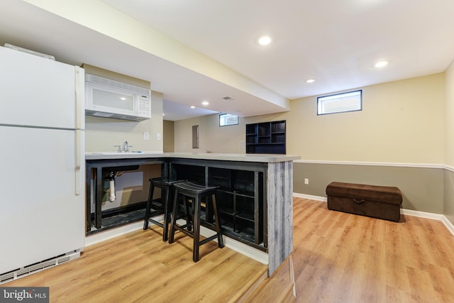 kitchen with white appliances, kitchen peninsula, light hardwood / wood-style flooring, a breakfast bar, and sink