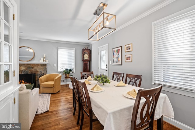 dining space with a fireplace, wood-type flooring, a notable chandelier, and ornamental molding