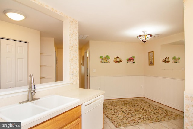 kitchen featuring light tile patterned flooring, a sink, light countertops, wainscoting, and dishwasher