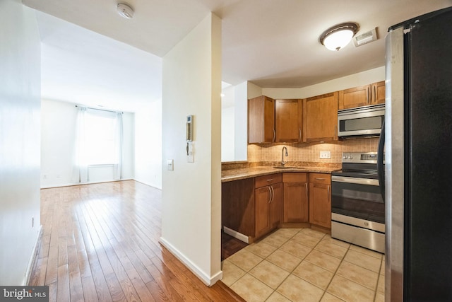 kitchen featuring backsplash, sink, stainless steel appliances, and light hardwood / wood-style flooring