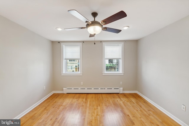 spare room with ceiling fan, light wood-type flooring, and a baseboard heating unit