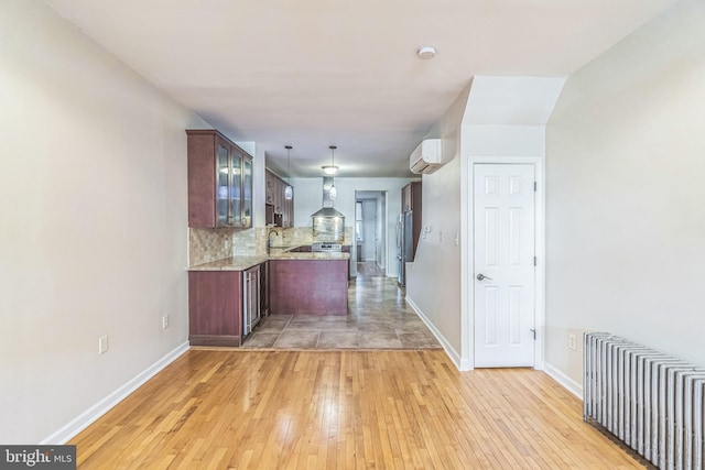 kitchen featuring light stone countertops, wall chimney exhaust hood, tasteful backsplash, pendant lighting, and light hardwood / wood-style floors