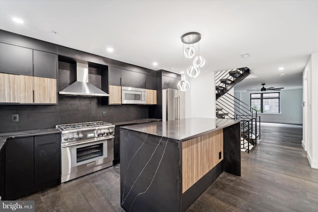 kitchen with a center island, high quality appliances, wall chimney range hood, ceiling fan, and decorative backsplash