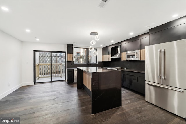 kitchen featuring stainless steel appliances, wall chimney range hood, dark hardwood / wood-style flooring, decorative light fixtures, and a kitchen island