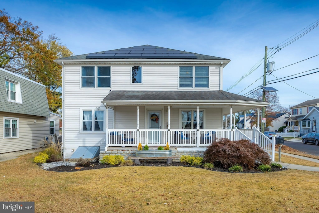 view of front of property with a front yard, solar panels, and covered porch