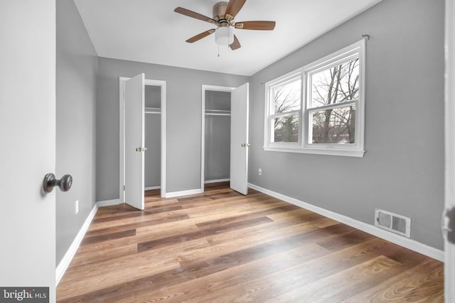 unfurnished bedroom with multiple closets, ceiling fan, and hardwood / wood-style flooring