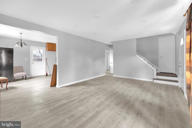 unfurnished living room featuring a notable chandelier and light wood-type flooring