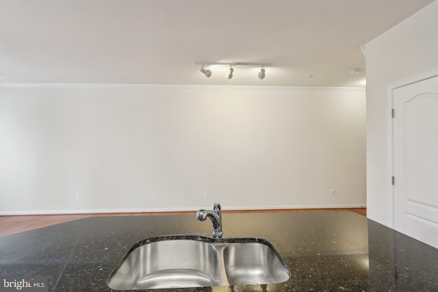 kitchen featuring track lighting, ornamental molding, dark stone counters, sink, and wood-type flooring