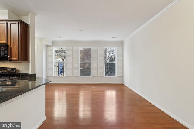 kitchen with crown molding, light hardwood / wood-style flooring, dark stone counters, and black appliances