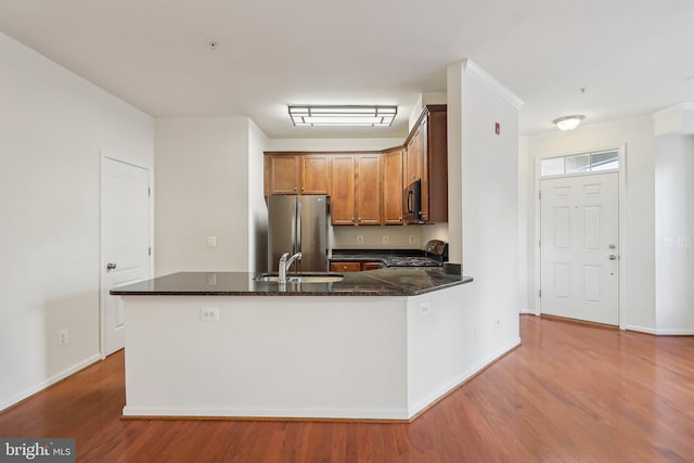 kitchen featuring kitchen peninsula, stainless steel fridge, sink, hardwood / wood-style flooring, and range