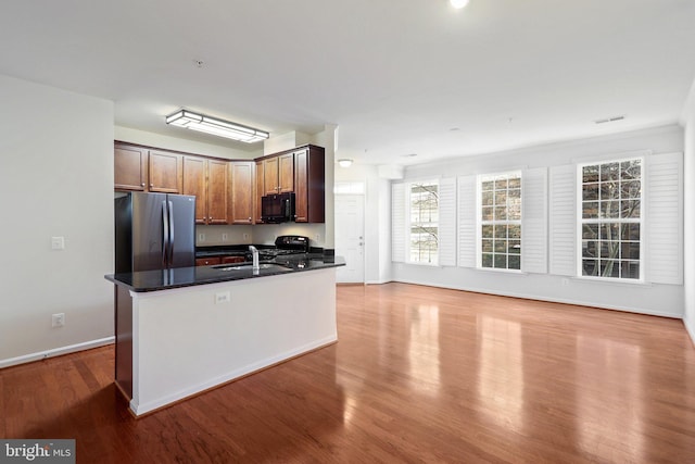 kitchen featuring sink, hardwood / wood-style flooring, dark stone counters, and black appliances