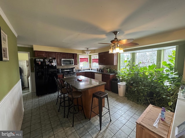 kitchen with a kitchen bar, ceiling fan, stainless steel appliances, ornamental molding, and a kitchen island