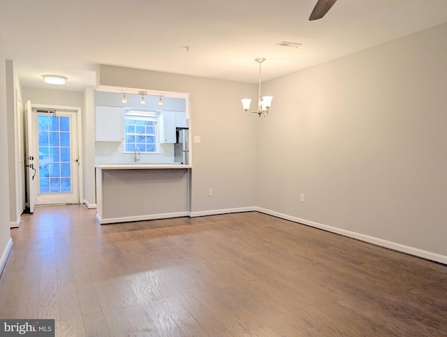 interior space featuring white cabinetry, hanging light fixtures, stainless steel fridge, decorative backsplash, and hardwood / wood-style flooring