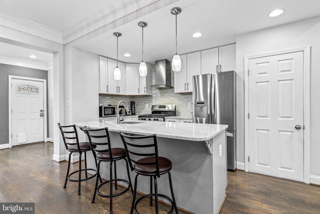 kitchen with appliances with stainless steel finishes, white cabinetry, a center island with sink, decorative light fixtures, and wall chimney exhaust hood