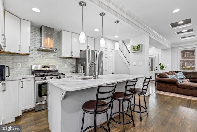 kitchen with sink, stainless steel appliances, white cabinets, a center island with sink, and wall chimney exhaust hood