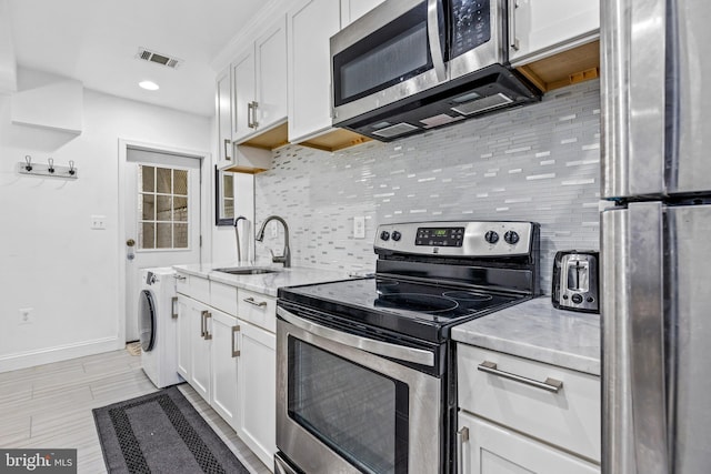 kitchen featuring sink, appliances with stainless steel finishes, white cabinetry, tasteful backsplash, and washer / clothes dryer