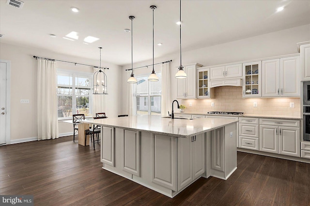 kitchen with an island with sink, sink, white cabinets, stainless steel appliances, and light stone countertops